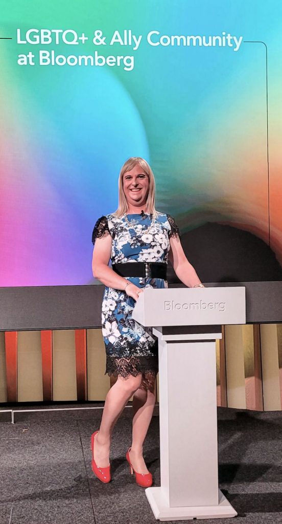 Pips Bunce standing behind the podium on the main London Auditorium stage at the Bloomberg HQ as part of the LGTBQI+ Pride flagship event, discussing identities
