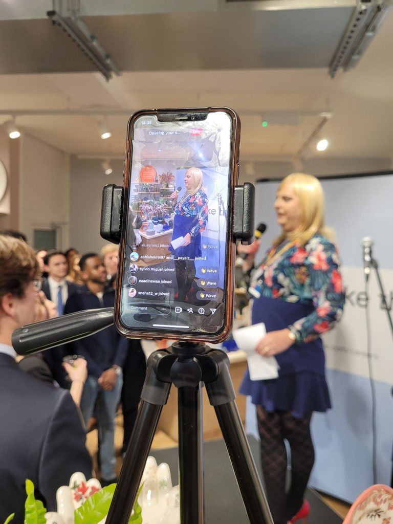 Pips Bunce standing on stage addressing the crowd as part of a HubDot event. In this, she is talking to students and interns who are looking to enter the corporate professional world.