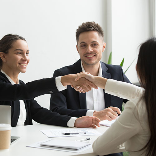 A group of people at a table shaking hands to depict the advisory and strategy services offered.